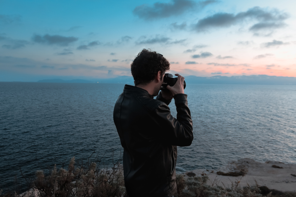 Back view of a young photographer taking pictures of the ocean