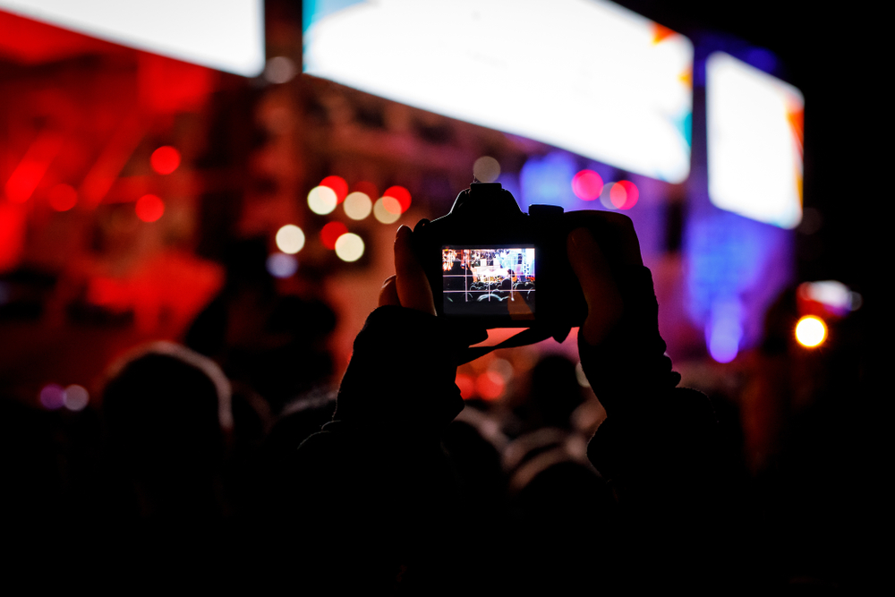 camera at a concert in raised hands recording singer on a stage