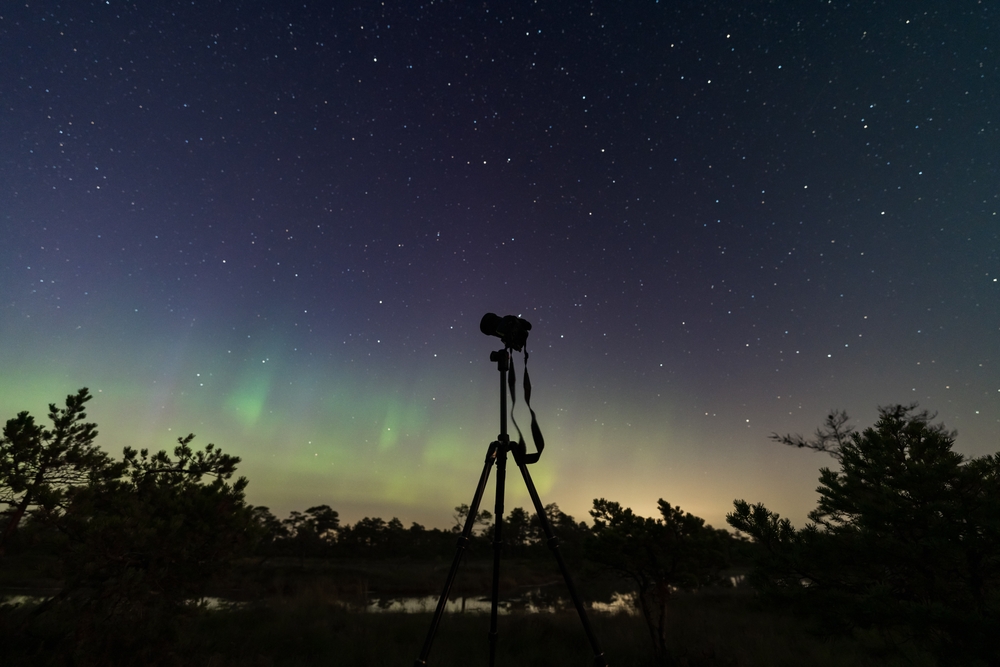 camera on a tripod during the northern lights and starry sky
