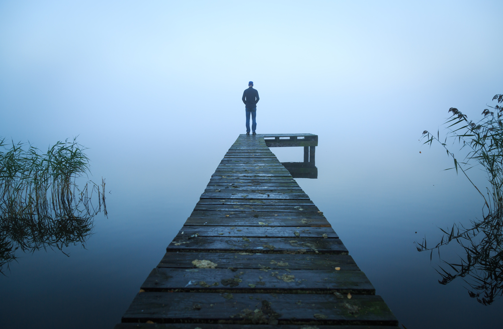 man standing at the end of a jetty on a foggy autumn morning