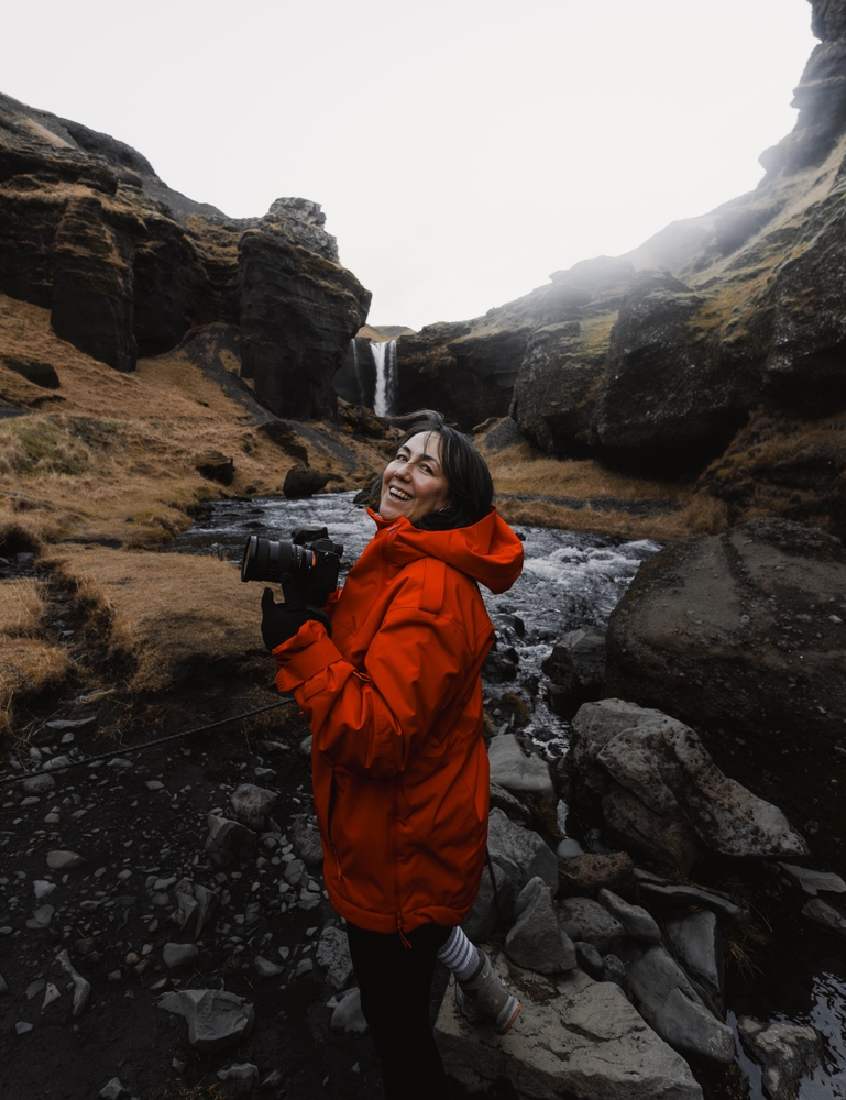 photographer smiling while holding camera near waterfall