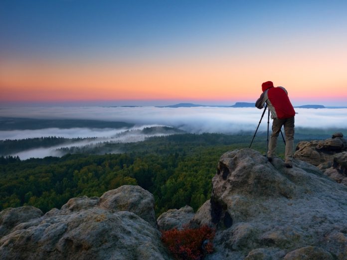 Photographer taking photos tripod on peak of rock